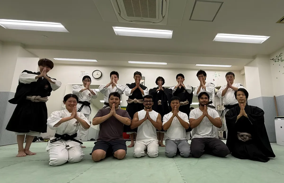 Participants and instructors in two rows on the dojo mats, kneeling in front and standing behind, all with palms pressed together in the Shorinji Kempo greeting