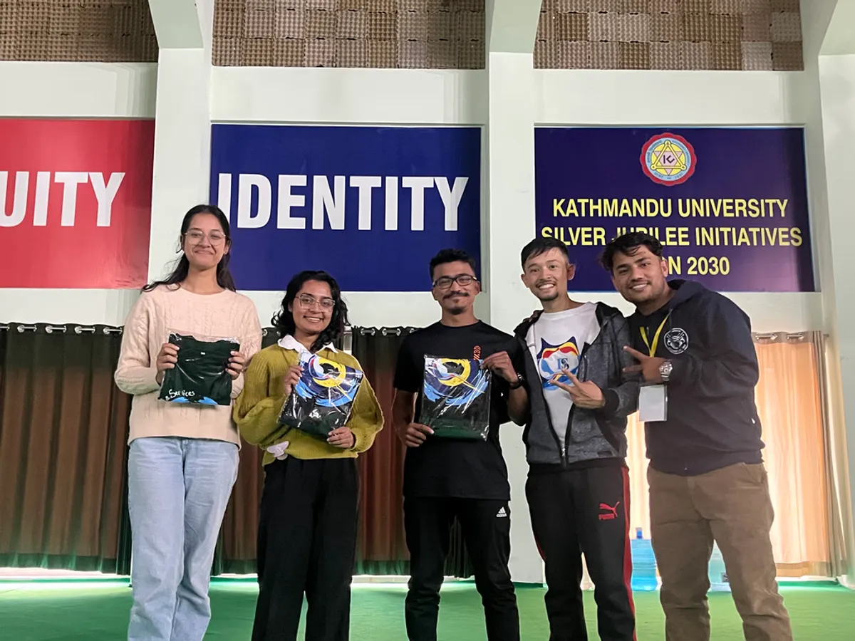 Five students on stage holding D&S goodie bags in front of the Kathmandu University Silver Jubilee backdrop