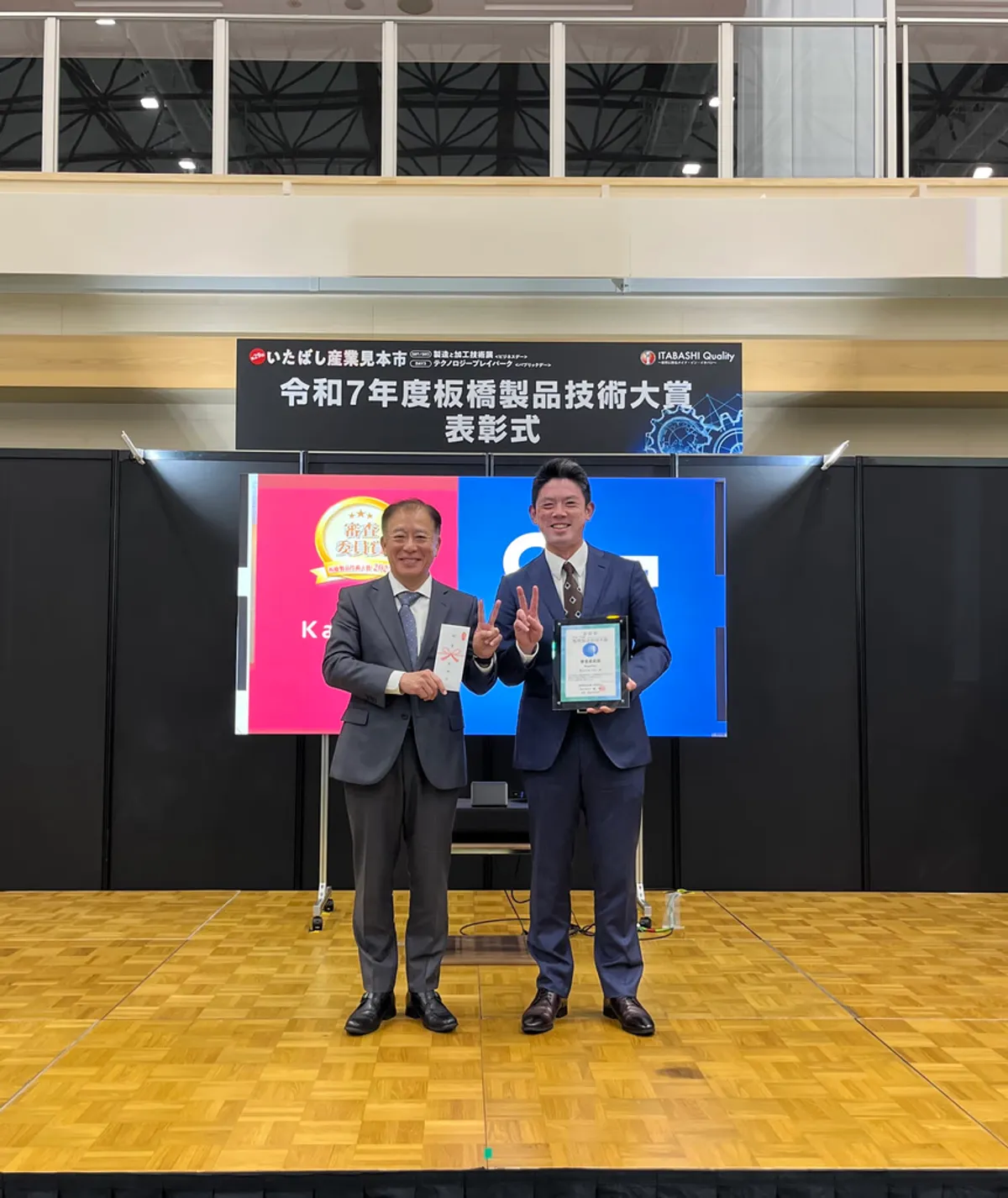 Two D&S representatives on stage at the award ceremony, holding the Itabashi Product Technology Award certificate and trophy