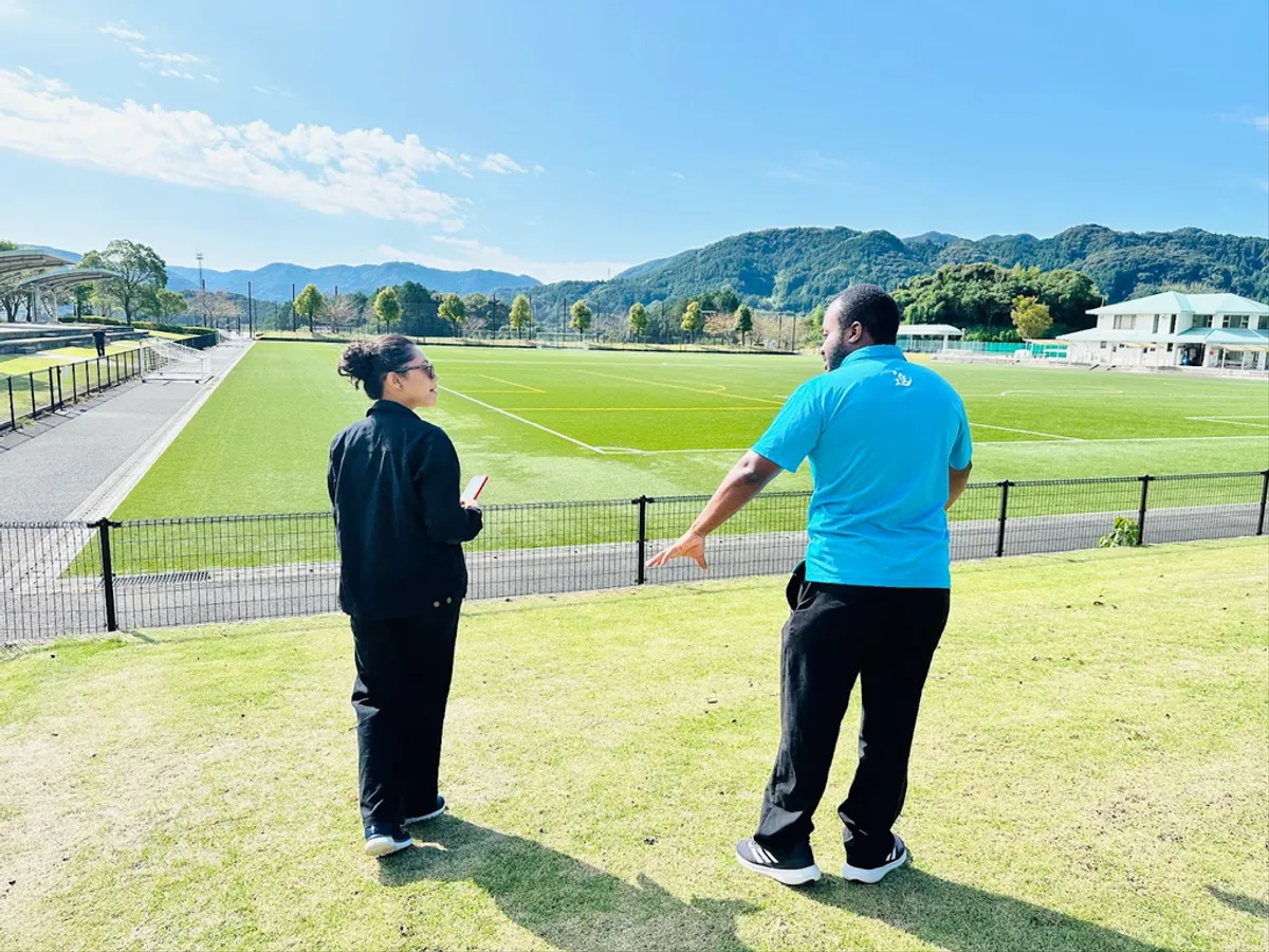 Two D&S staff talking beside a green sports field with mountains in the background